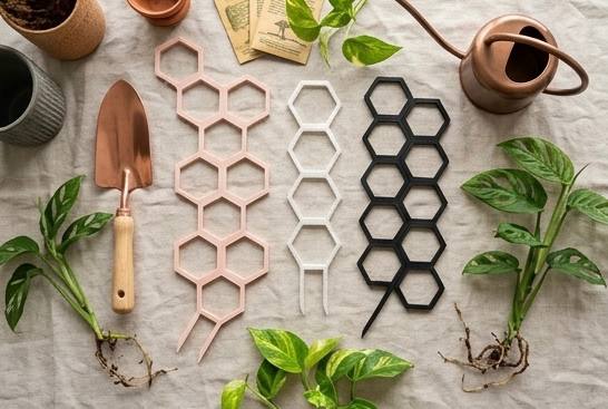 Stackable 3D printed plant trellises shown flat in blush, white, and black with plant cuttings and garden tools