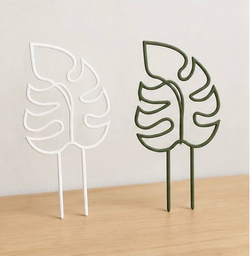 White and green monstera leaf shaped 3D printed plant trellises on a tabletop