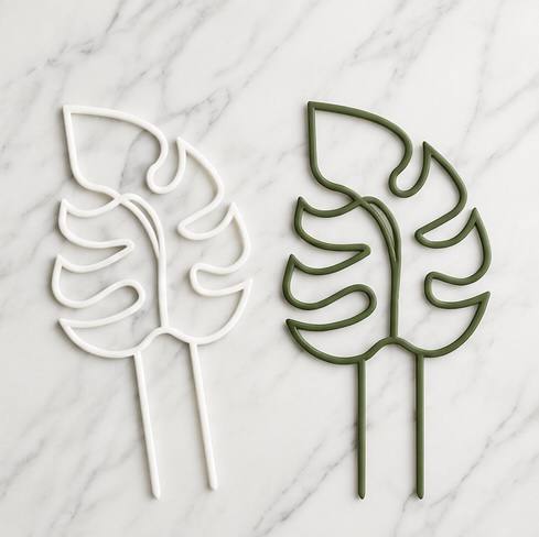 White and green monstera leaf shaped 3D printed trellises laid flat on a marble surface